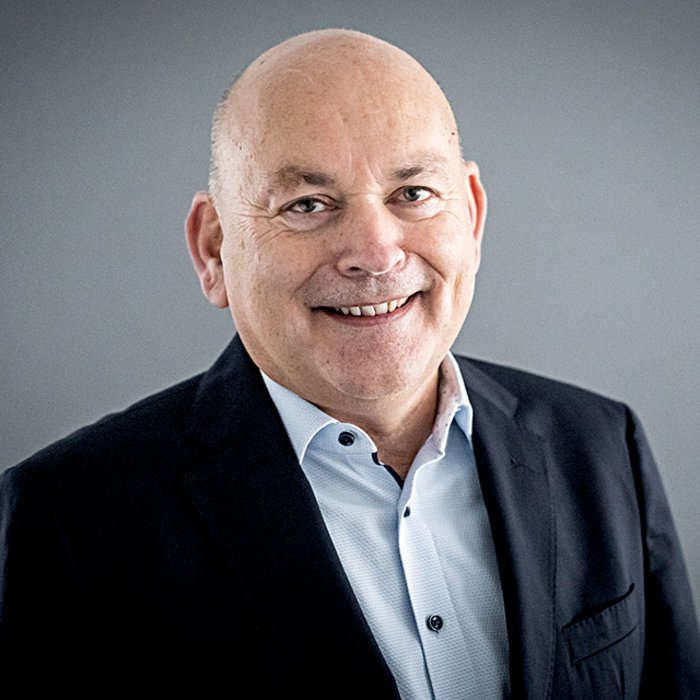 Geschäftsführer des Sozialkontor, Kay Nernheim, lächelt freundlich in die Kamera. Er trägt ein helles Hemd und einen dunklen Anzug. Der Hintergrund ist neutral grau gestaltet.