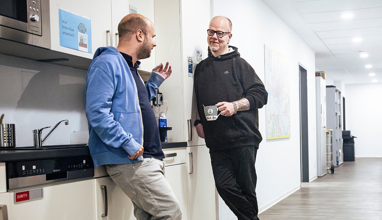 Niklas Luy und ein Kollege unterhalten sich in der Teeküche ihres Büros bei GUT GEFRAGT.