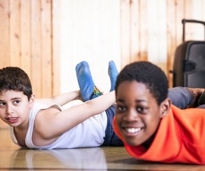 Zwei Förderschüler liegen lachend auf dem Boden einer Turnhalle und machen eine Bewegungsübung.
