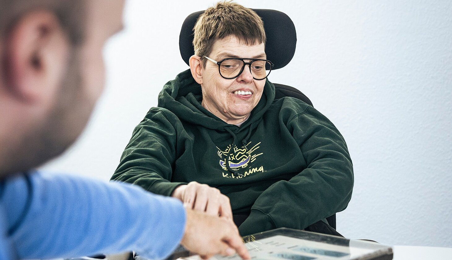 Eine Person mit Behinderung wird von einer anderen Person befragt und zeigt etwas auf einem Tablet.