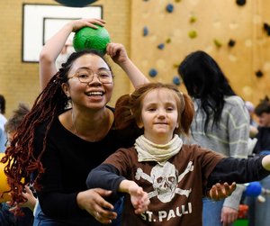 Mitarbeiterin lacht mit einer Förderschülerin beim Ballspiel in der Sporthalle.